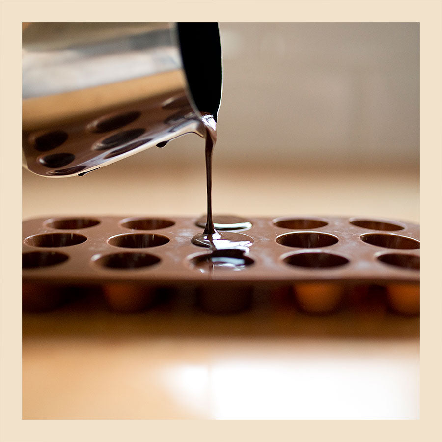 pouring raw chocolate from a jug into a silicone chocolate mould